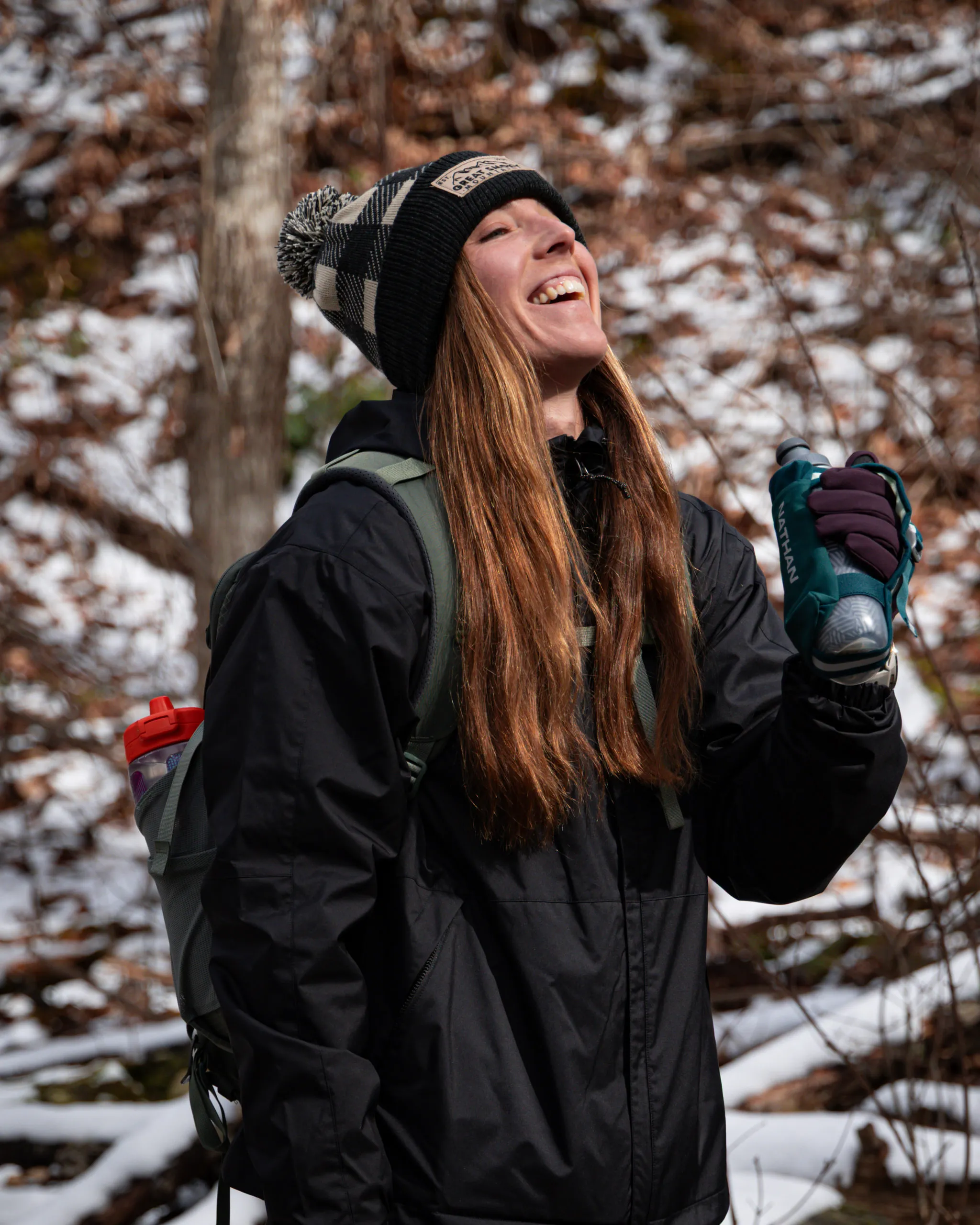 A runner laughing on a snowy winter trail, pack on