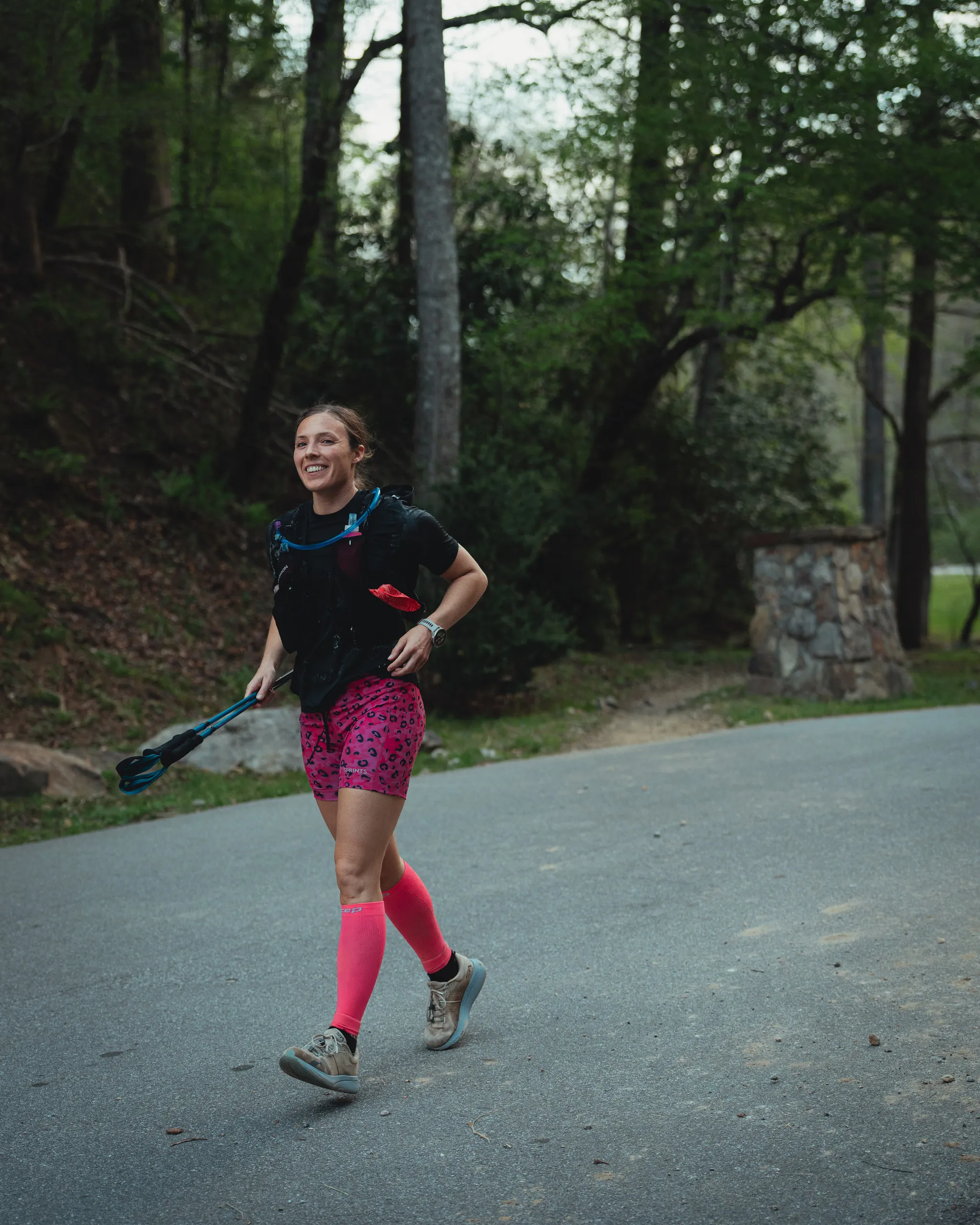 Lexi running a mountain ultra marathon, smiling, trekking poles in hand